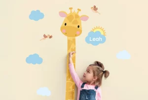Kind, das seine Größe an einer Messleiste mit Giraffenmotiv und dem Namen „Leah“ misst.