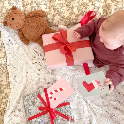 Baby, das sitzt und Geschenke mit roten Schleifen und Weihnachtskarten anschaut.