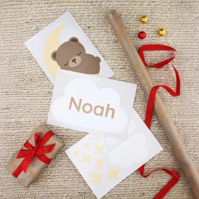 Türsticker auf einem Bogen mit einem Bären, der auf einem Mond schläft, und einer Wolke mit teksten "Noah", umgeben von Geschenkpapier zu Weihnachten.