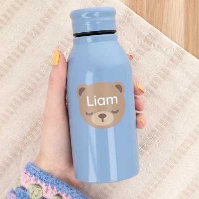 Trinkflasche in der Hand mit einem großen Namensaufkleber mit Bärenmotiv und dem Namen „Liam“.