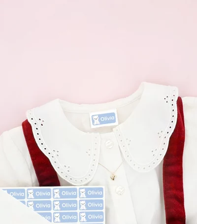 Kinderschuhe und Kinderkleid mit Namensaufklebern auf der Kleidung, umgeben von Schneeflocken-Deko.