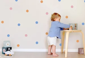 Kleinkind spielt im Kinderzimmer mit bunter Wanddekor aus Punkten, ideal für kreative Raumgestaltung mit personalisierten Designs.