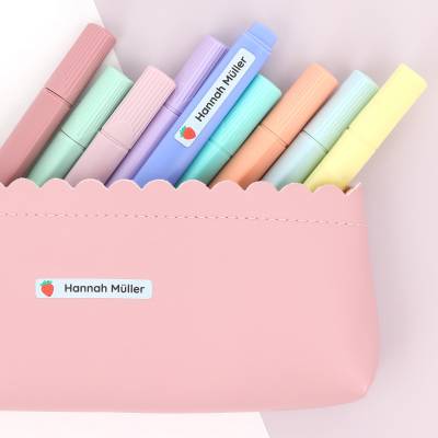 Alt-teksten kan være:Personlige navnelapper med navnet 'Hannah Müller' på et rosa penal med fargerike tusjer, ideelt for barn og deres kreative prosjekter.