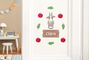 Bunte Wanddekoration für Kinder mit einer Ziege, roten Äpfeln und dem Namen „Clara“ auf einer Holzplakette. Perfekt für das Kinderzimmer und verleiht der Einrichtung eine persönliche Note.