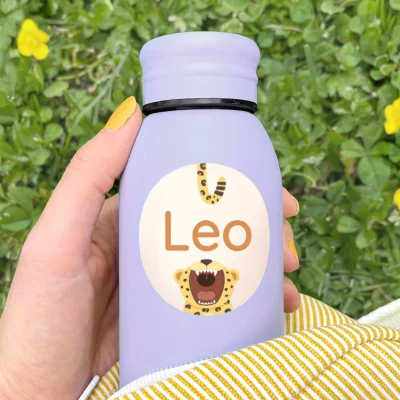 Person hält eine lilafarbene Wasserflasche mit personalisiertem Namensaufkleber „Leo“ und Leopardenmotiv – ideal für Kinder.