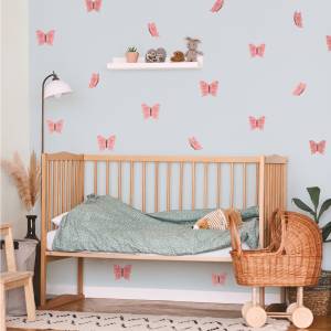 Ein Kinderzimmer mit einer holzfarbenen Wiege und grüner Bettwäsche. Die Wand ist mit rosa Schmetterlingen dekoriert, die dem Raum eine verspielte Note geben.