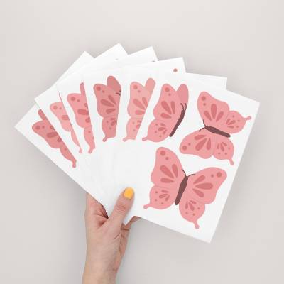 Hand hält einen Bogen mit Wandstickern mit blauem Schmetterlingsdesign, perfekt für Kinderzimmer.