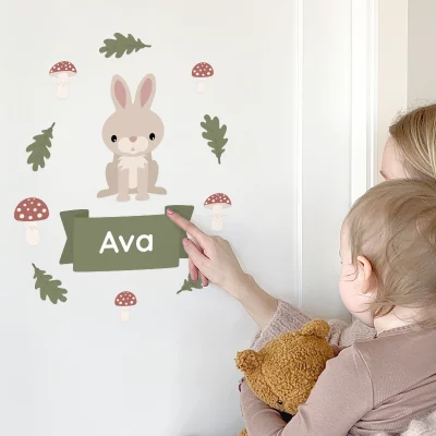 Türaufkleber mit Namen und einer süßen Kaninchenillustration für das Kinderzimmer, die eine Mutter zeigt, die auf die Dekoration zeigt, während sie ihr Kind und einen Teddybären hält. Perfekt zur Personalisierung des Zimmers für Kleinkinder.