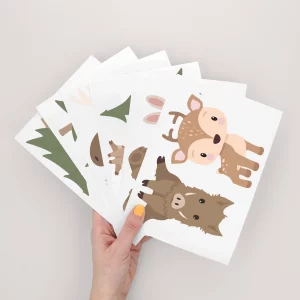 Eine Hand hält mehrere farbenfrohe Poster mit Tiermotiven, ideal als Wanddeko fürs Kinderzimmer. Diese grafischen Designs bringen Leben in jedes Kinderzimmer.