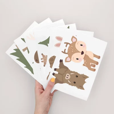 Eine Hand hält mehrere farbenfrohe Poster mit Tiermotiven, ideal als Wanddeko fürs Kinderzimmer. Diese grafischen Designs bringen Leben in jedes Kinderzimmer.