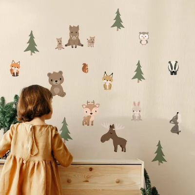 Ein kleines Mädchen steht vor einer Wand mit niedlichen Tiermotiven und Bäumen – perfekt fürs Kinderzimmer.