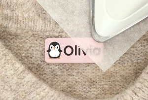 Personalisierte Namensetiketten mit einem niedlichen Pinguin-Design für Kinder. Ideal zum Beschriften von Kleidung, Spielsachen und mehr. Das Bild zeigt das Etikett auf einem weichen, strukturierten Untergrund.