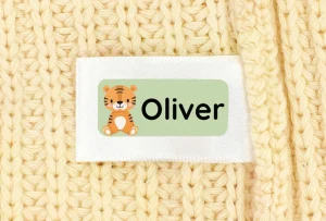 Personalisierte Namensetiketten für Kinder mit einem süßen Tiger und dem Namen „Oliver“ auf einem gestrickten Untergrund. Ideal für persönliche Gegenstände und als dekorative Elemente in Kinderzimmern.